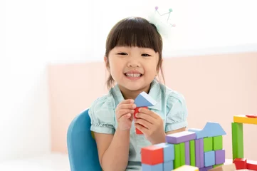 Fotobehang Lego Cute little Asian girl playing with colorful toy blocks while sitting at table and smiling at the camera. Educational and creative toys and games for young children. Child at home.  © edward_indy