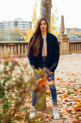 Attractive young woman with long hair in winter clothes poses for the camera in a park in autumn or spring.
