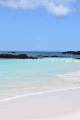 Sandy tropical beach and blue turquoise ocean water under blue sky and lava stones