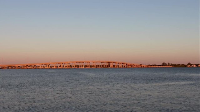 Sunset illuminating a bridge gold while cars are driving across the river from one city to another 4k Wide video adcopy