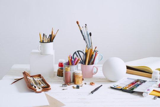 Interior of painting studio of freelance artist. Gypsum shapes, brushes, pencills, ink and paint bottles with sketchbooks on the table. Freelance artist lifestyle concept. Copy space
