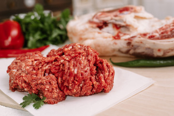 Red fresh minced meat on the background of lamb legs, red pepper and greens. Ground beef on the background of fresh meat in the kitchen of a housewife