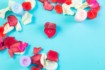 Heart of rose petals on a blue background and a box with jewelry.