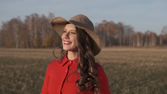 Young happy beautiful smiling traveler tourist woman girl in red dress and hat with retro suitcase at outdoors walking in summer rural road. Travel happiness tourism trip nature vacation. 4 K slow-mo