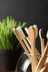Close up of several biodegradable bamboo toothbrushes in a glass cup on a dark background. Image with copy space, vertical orientation. Zero waste concept.