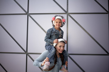 Fashion family dressed jeans wear and walking together in the street of the city. Poeple wearing denim clothes. Mother holding daughter on shoulder and posing at the background wall