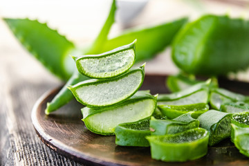 Slices of aloe vera in a bowl on a wooden table. - obrazy, fototapety, plakaty
