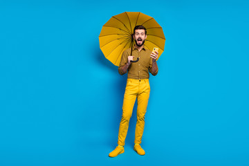 Full length photo energetic guy use smartphone get comment impressed scream omg hold protect rainstorm shield parasol wear style stylish trendy checkered pants isolated blue color background © deagreez