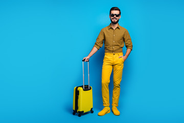 Full size photo positive bearded guy tourist enjoy air voyage stand in terminal wait check-in hold total yellow rest look trolley wear plaid clothes sneakers isolated blue color background