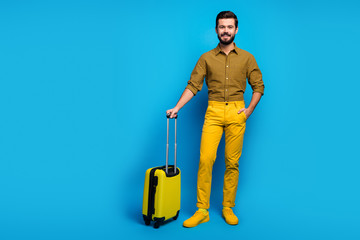 Full length photo of positive cheerful guy have big bright bag trolley enjoy tourism weekend wear good look trendy clothing gumshoes isolated over blue color background