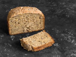 Half a loaf of homemade whole grain bread with various seeds and two slices on a black background