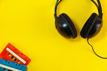 Top view of Headphone and blue classic tape cassette against yellow isolated background. Listening music theme.