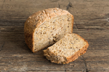 Half a loaf of homemade whole grain bread with various seeds and two slices on a wooden background