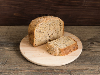 Half a loaf of homemade whole grain bread with various seeds and two slices on a wooden background