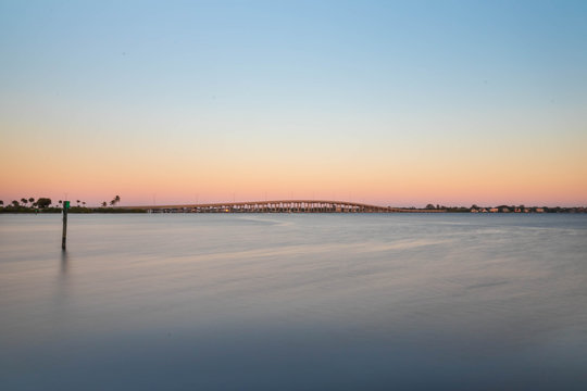 Sunset illuminating a bridge gold while cars are driving across the river from one city to another