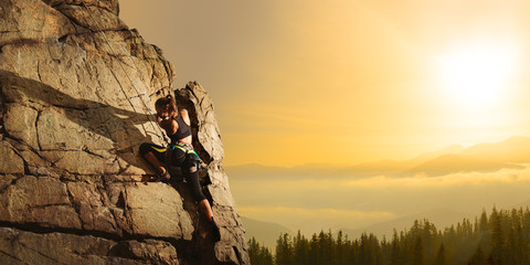 Beautiful Woman Climbing on the Rock at Foggy Sunset in the Mountains. Adventure and Extreme Sport...