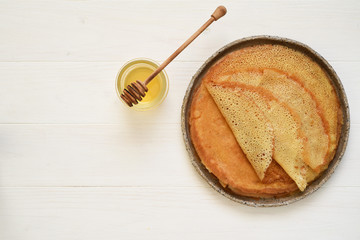 Thin crepes with honey on a white wooden background.