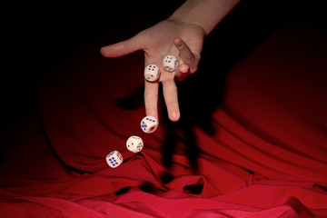 Hand throwing gambling dice on  table, red fabric background 
