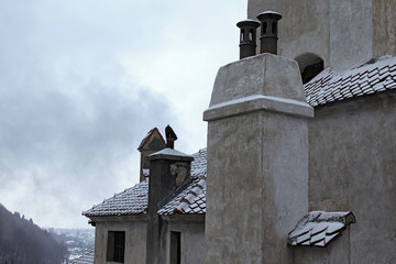 Close up view of roof covered by red tile in the snow with several chimneys. Ancient Bran Castle,...