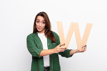 young pretty woman confused, doubtful, thinking, holding the letter W of the alphabet to form a...