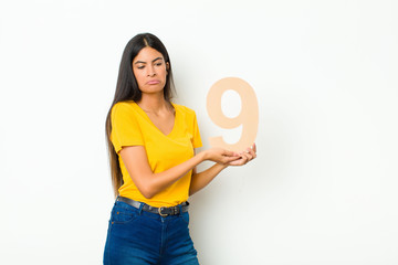 young latin pretty woman sad, depressed, unhappy, holding a number 9.