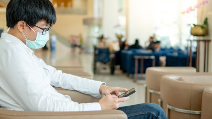 Male Asian patient wearing surgical mask using smartphone in hospital or medical center. Medical...