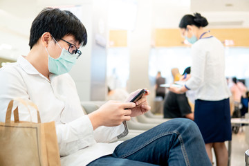 Male Asian patient wearing surgical mask using smartphone in hospital or medical center. Medical...