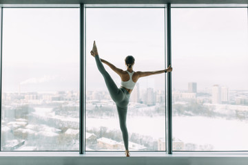 Fototapeta na wymiar Stretching in the white room by the window. Beautiful girl athlete on the Mat. Flexibility exercises on a light background.