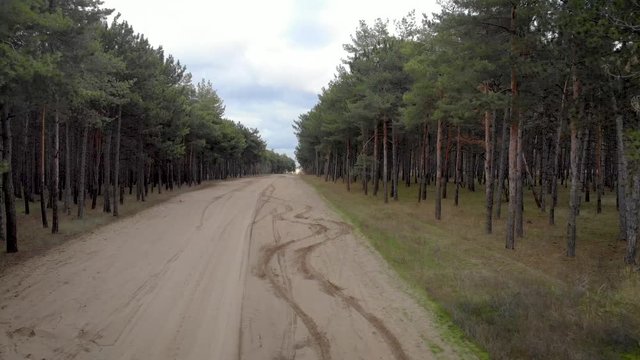 Aerial view from quadro copter on woods road with tire tracks from cars on road. Cinematic drone shot video of flight over gravel sandy road in pine forest