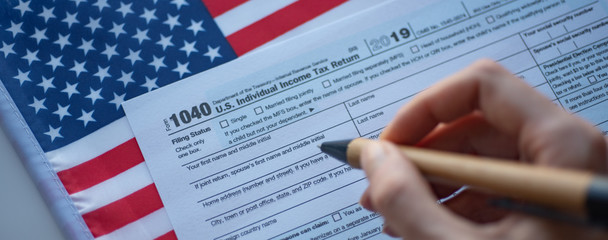 Form 1040 U.S. Individual  Income Tax return and hand with pen on flag of USA background. Wide photo. Close up view.