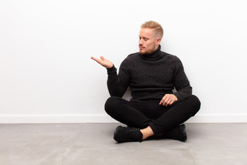 young blonde man feeling happy and smiling casually, looking to an object or concept held on the...