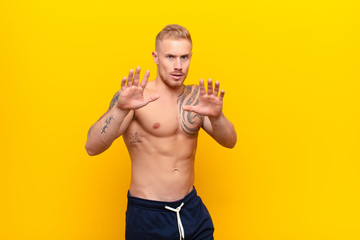 young strong blonde man feeling terrified, backing off and screaming in horror and panic, reacting...