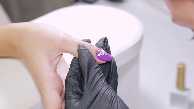 Manicurist woman in a beauty salon decorates client's nails with gel varnish with rhinestones