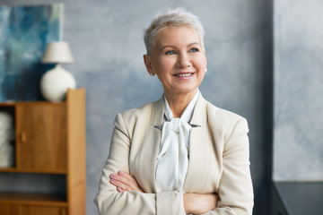 Attractive successful female professional in her fifties posing in office interior wearing stylish...