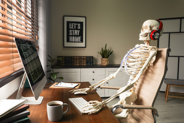 Human skeleton with headphones using computer at workplace - obrazy, fototapety, plakaty