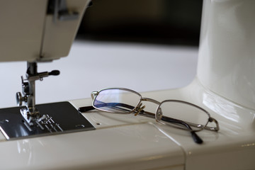 Glasses for vision lie on the platform of the sewing machine. Selective focus.