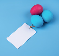 colored eggs with blank white tag isolated on blue background top view