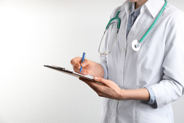 Doctor with stethoscope and clipboard on white background, closeup. Medical service