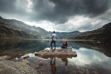 A woman and man stands on a rock on the lake. Mountain view. Valley of Five Ponds in the Tatra mountains.
