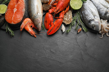 Fresh fish and different seafood on black table, flat lay. Space for text