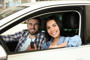 Happy couple with car key sitting in modern auto at dealership