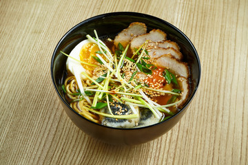 Traditional thai ramen soup with noodles, meat, shiitake mushrooms and egg in a black bowl on a wooden background. Delicious food close up