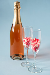 Two champagne glasses with red heart shaped sugar candy and champagne bottle. On blue background. Valentines Day, anniversary or wedding celebration concept.  Copy space.