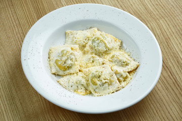 Appetizing and homemade ravioli stuffed with mushrooms or meat and ricotta cheese on a white plate on a wooden background. Italian Cuisine. Close up food