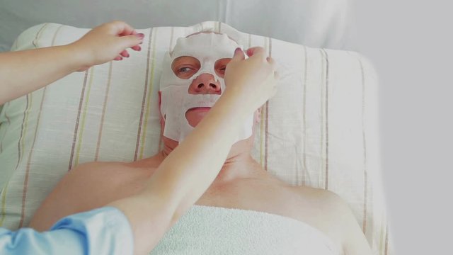 A female beautician removes a moisturizing face mask from a client in a spa salon