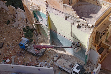 Fototapeta na wymiar Aerial view of a workman on a hydraulic platform filling in cracks on a demolished building in Sliema, Malta