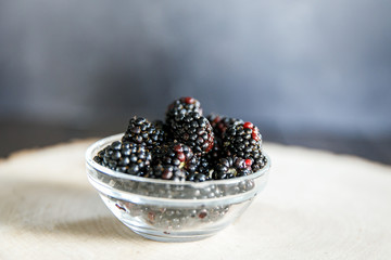 a clear glass bowl of fresh organic blackberries spilled out on a piece of cut wood