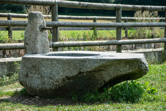 Grauer Steinbrunnen mit laufendem Wasser vor einem Holzzaun