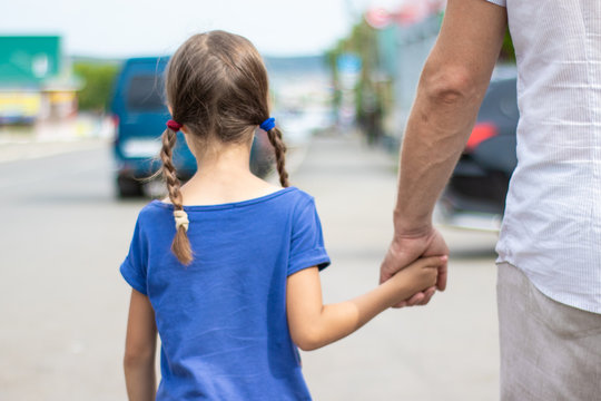 A man in bright clothes leads a little girl by the hand along the street