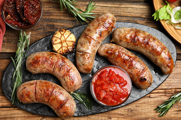 Tasty grilled sausages served on wooden table, flat lay